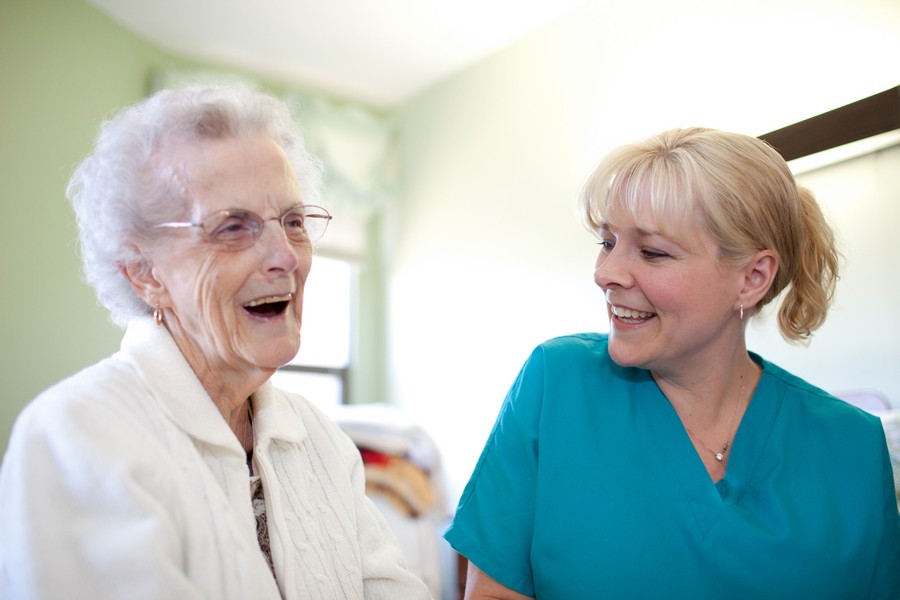 An elderly woman sharing a joyful moment with a caregiver.