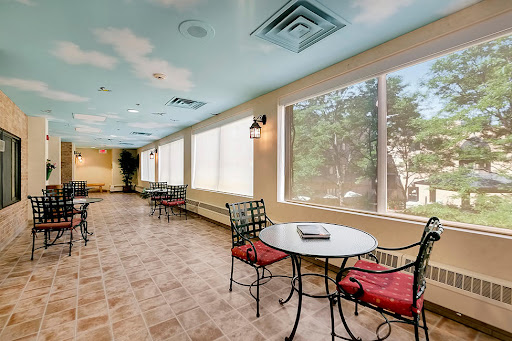 A cozy lounge area featuring tables and chairs, brightened by natural light streaming through large windows.