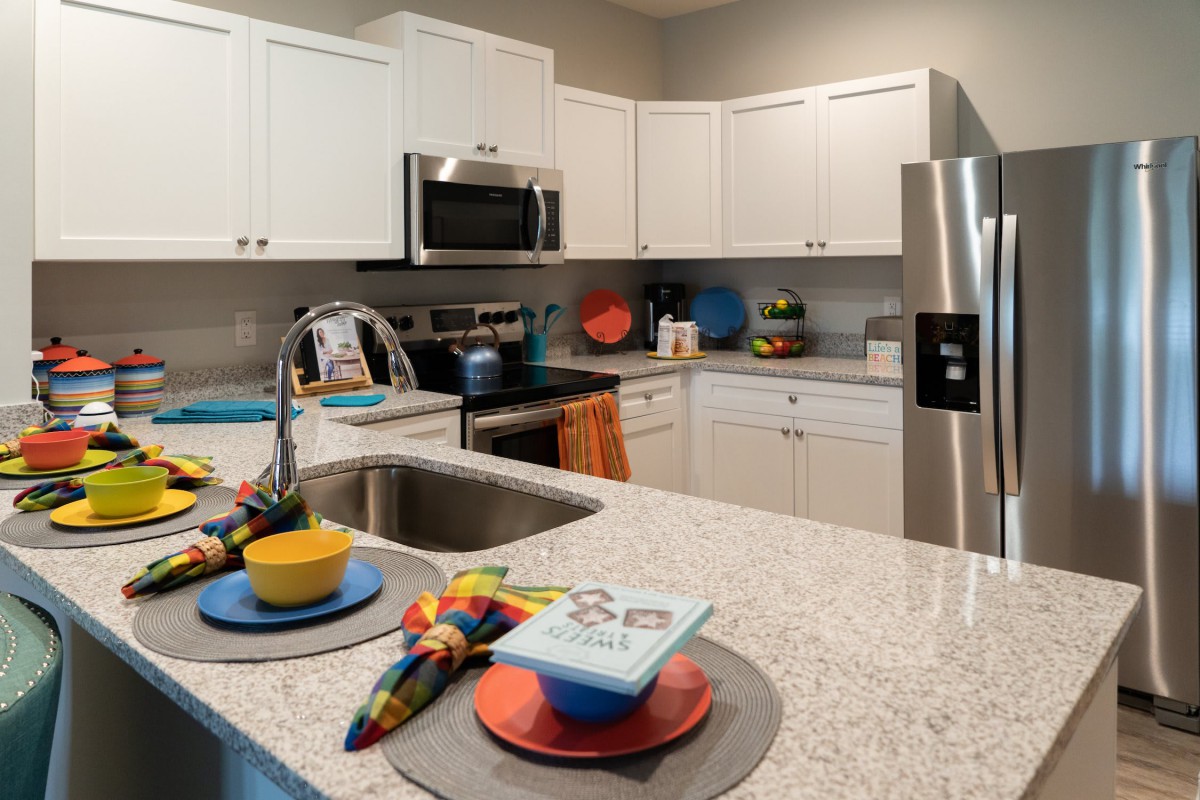 A modern kitchen with white cabinets and stainless steel appliances, featuring a decorated countertop with colorful dishware.