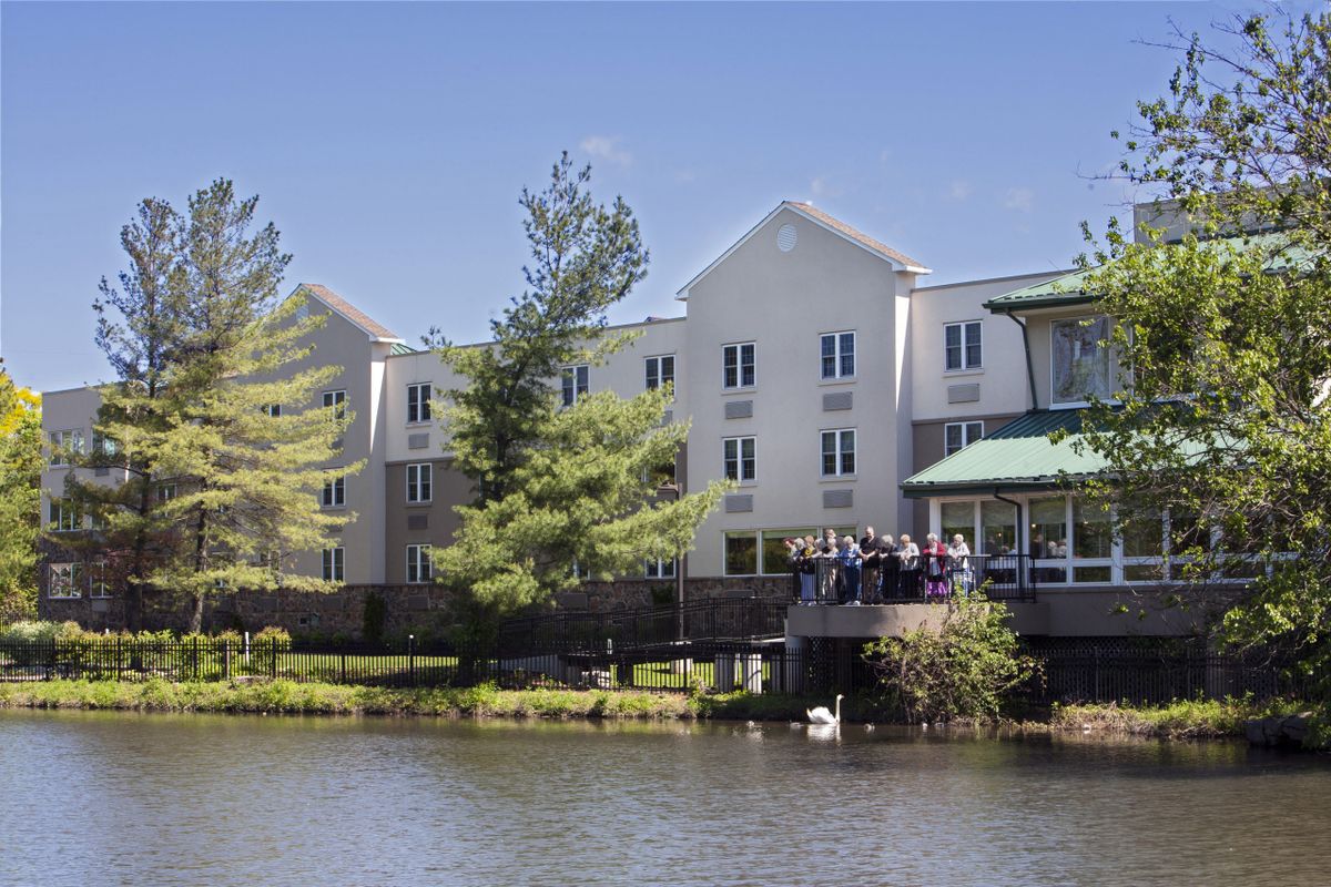 A scenic view of a building by the lakeside with surrounding trees under a clear blue sky.