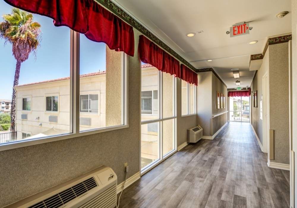 A brightly lit hallway with large windows, red curtains, and wood flooring.