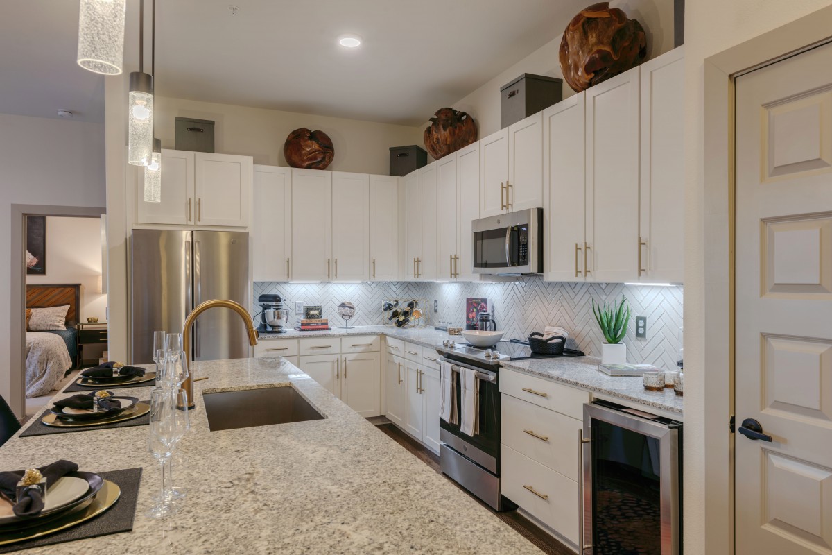 A modern kitchen featuring white cabinets, stainless steel appliances, and a granite countertop with decorative vases on top.