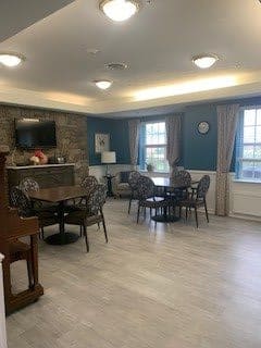 A cozy communal living space with tables, chairs, a piano, and a television.