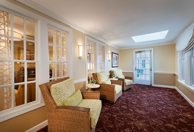 A cozy seating area with wicker chairs and a patterned carpet, featuring warm lighting and large windows.