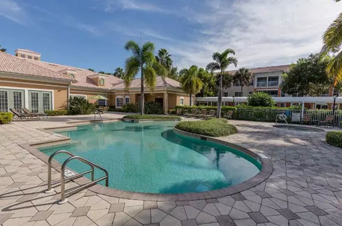 A luxurious resort with a sparkling swimming pool surrounded by palm trees on a sunny day.
