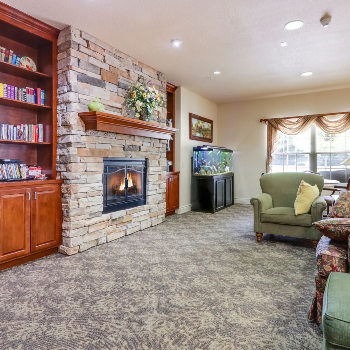 A cozy living room featuring a stone fireplace, built-in bookshelf filled with books, and an aquarium next to a comfortable armchair.
