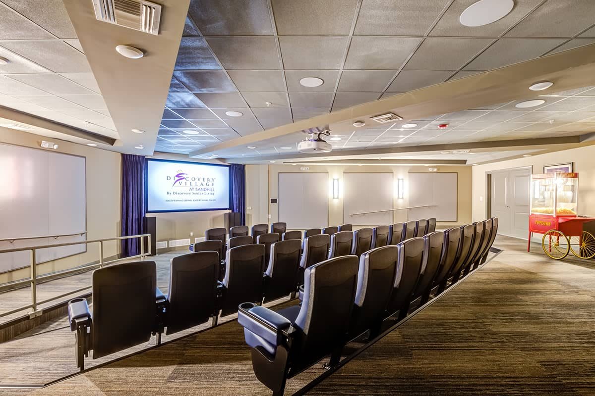An empty theater with rows of seats facing a projection screen.