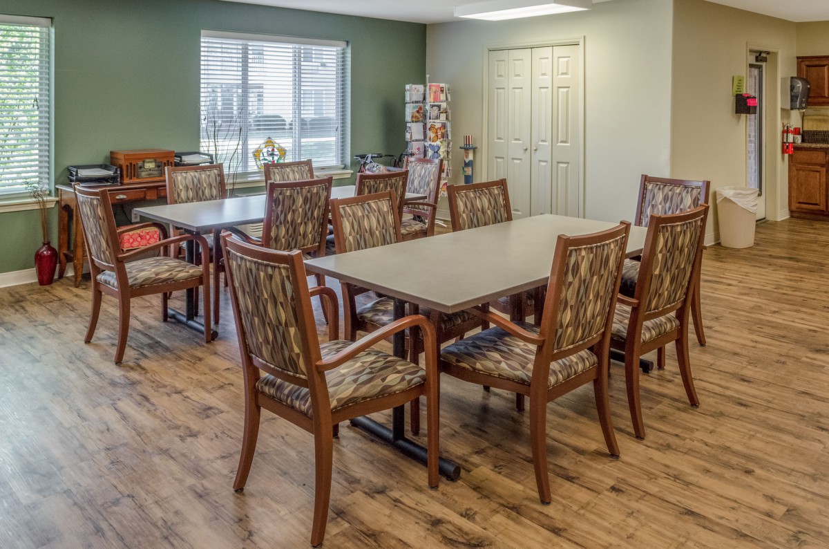 A neatly arranged dining or meeting room with tables and chairs on a wooden floor, featuring a large window for natural light.