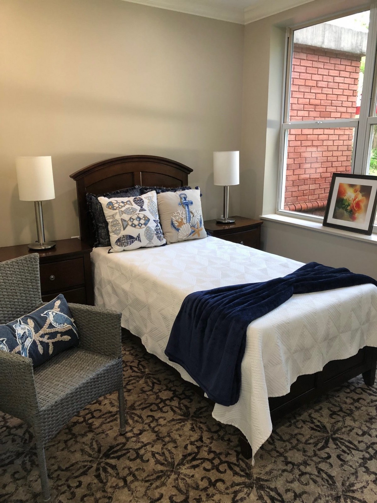A cozy bedroom with a neatly made bed, decorated with pillows and a dark blue throw, accompanied by a chair and two lamps.