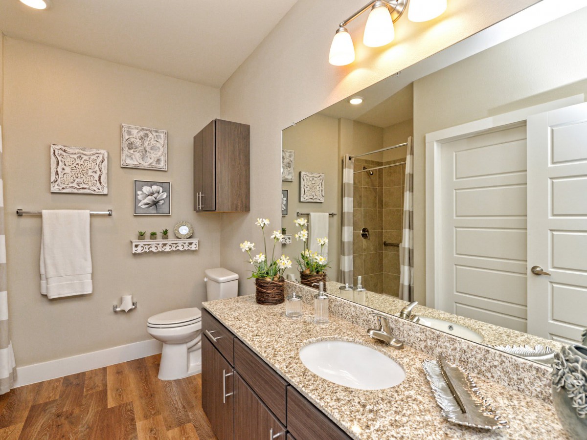 A modern bathroom interior featuring a granite countertop, large mirror, and contemporary lighting.