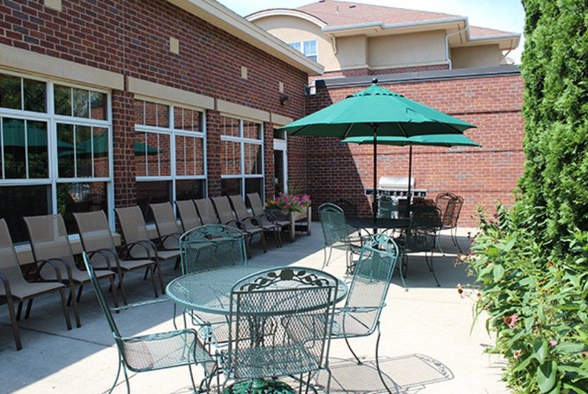 A sunny patio area with tables, chairs, and umbrellas next to a brick building.