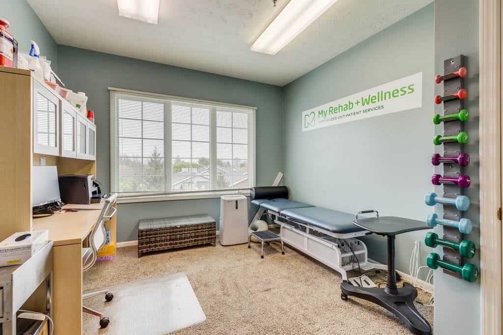 A clean and organized medical exam room with a treatment table and large windows.