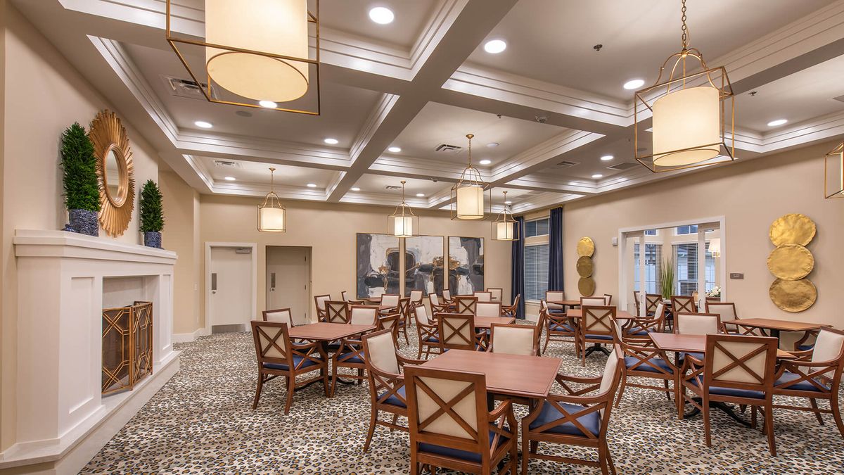 A spacious dining area with multiple tables and chairs, elegantly lit by ceiling lights.