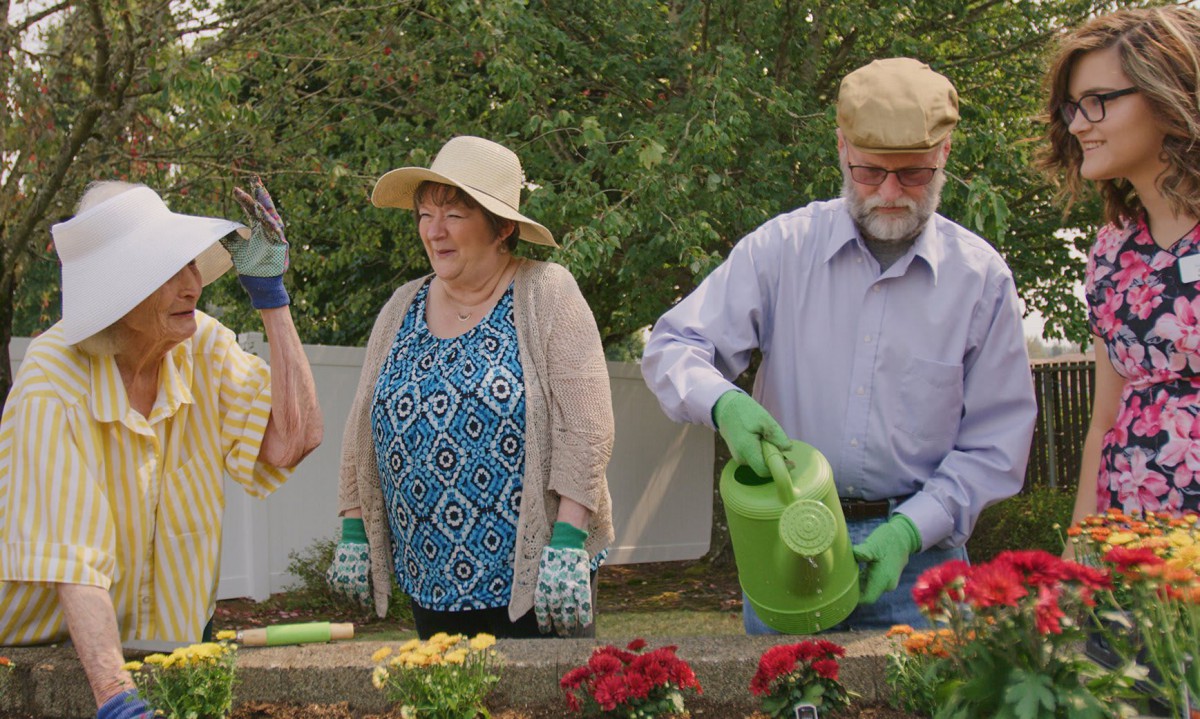 A group of mature adults gardening outdoors, wearing hats and gloves while tending to flowers.