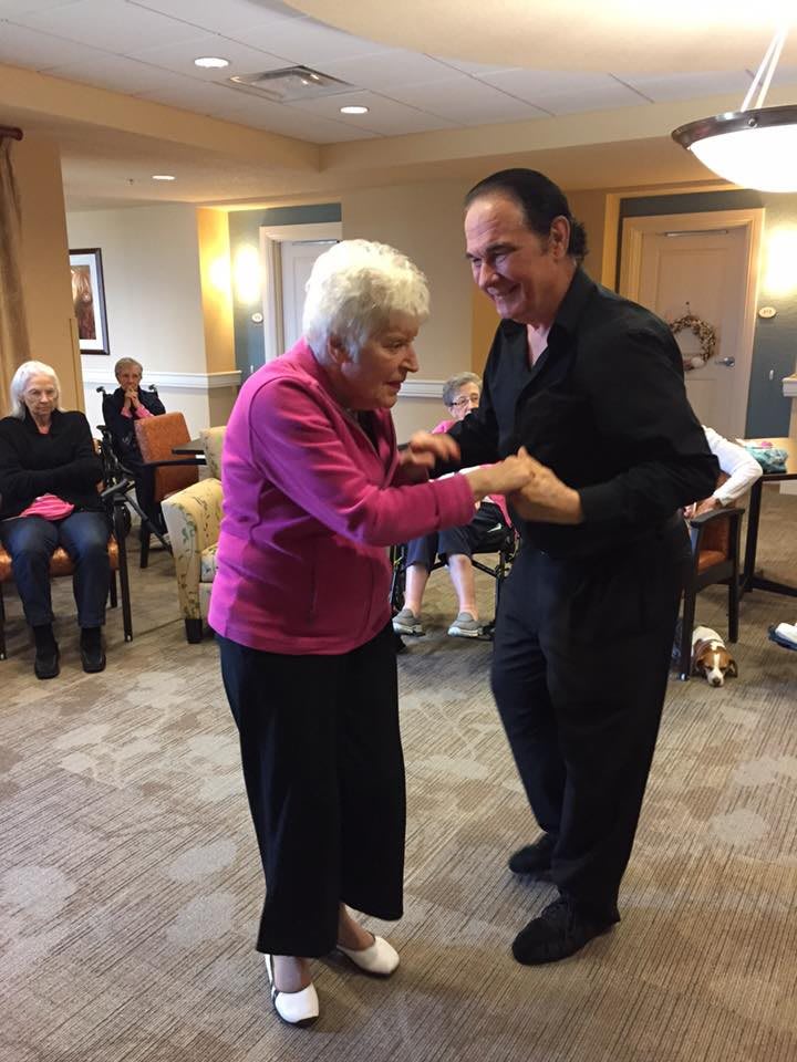 An elderly woman and a man enjoying a dance together in a communal setting.