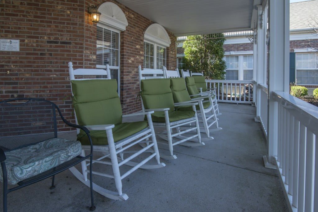 A row of white rocking chairs with green cushions on a covered porch.