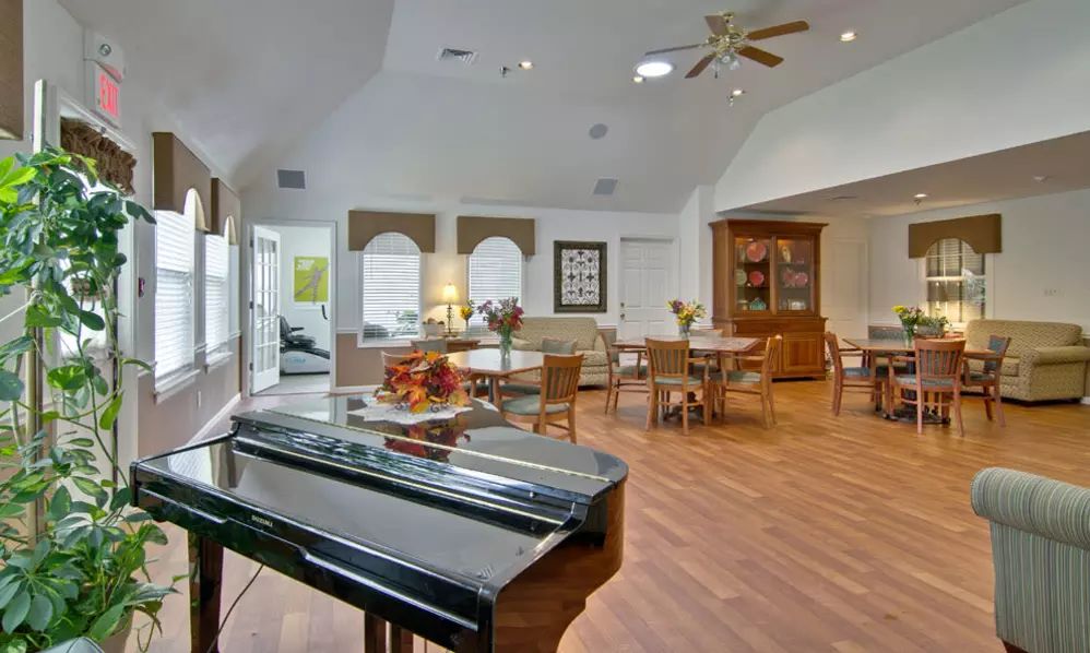 A spacious and well-lit living room featuring a piano, dining area, and wooden flooring.
