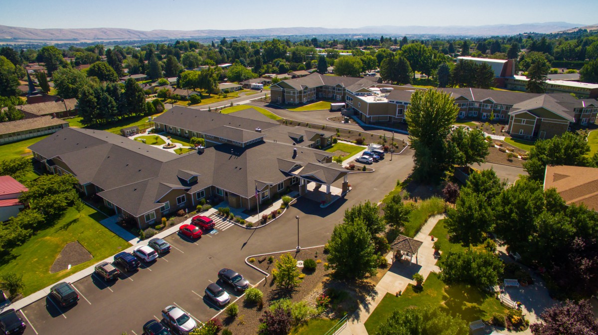Aerial view of a residential complex surrounded by greenery and parking spaces.