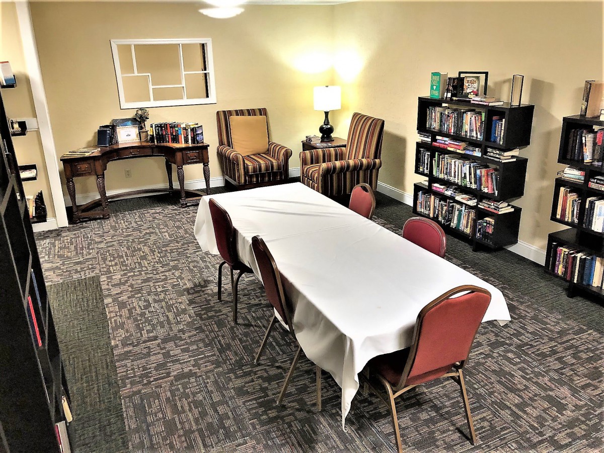 A cozy room with a table and chairs, bookshelves, and lamp.