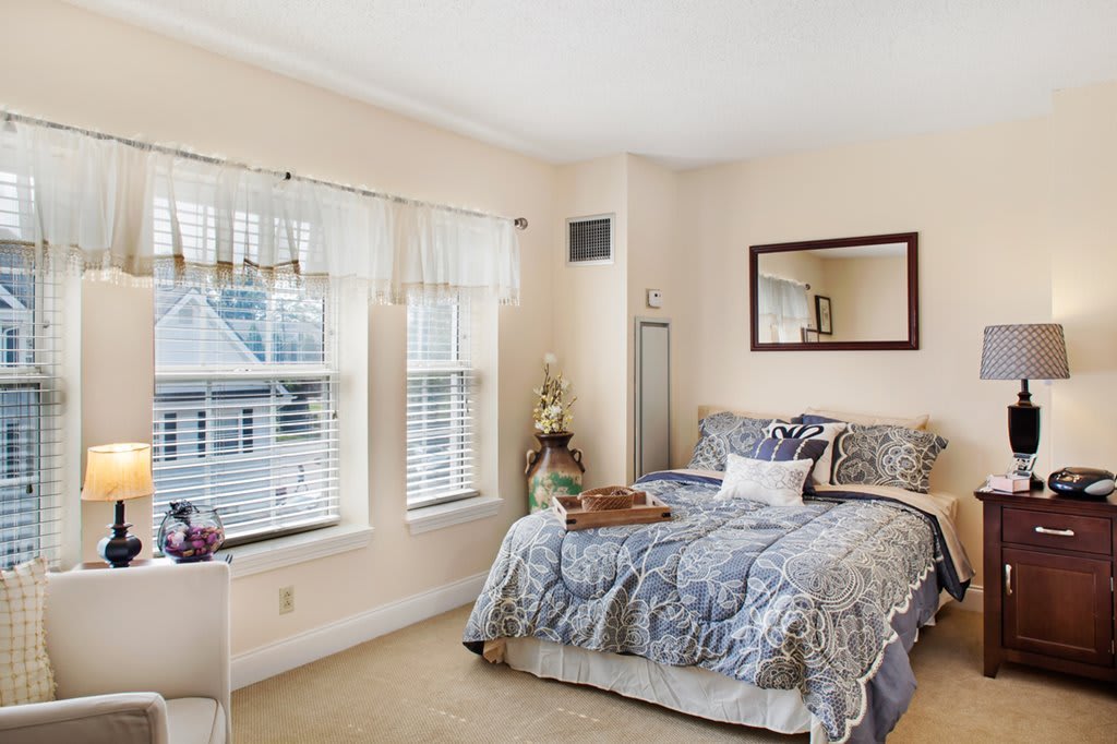 A cozy bedroom with a neatly made bed, large windows, and a wall mirror.