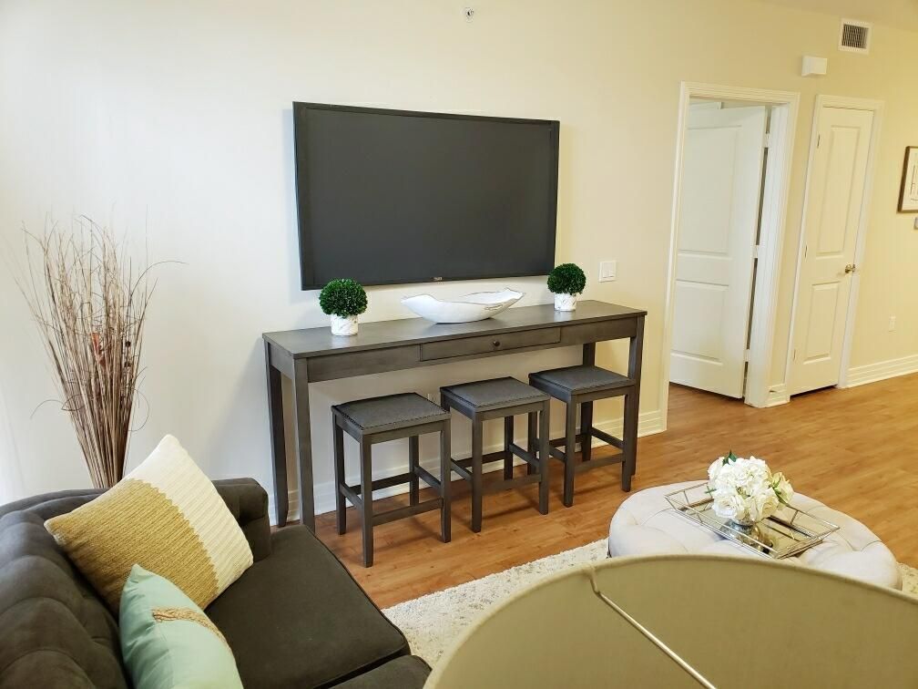 A modern living room with a mounted television above a console table and stools, accented by potted plants.