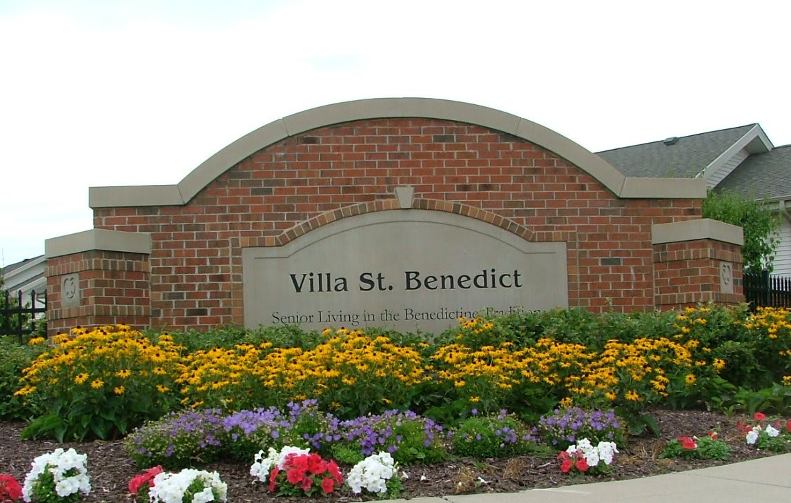 Entrance sign for Villa St. Benedict surrounded by colorful flowers.