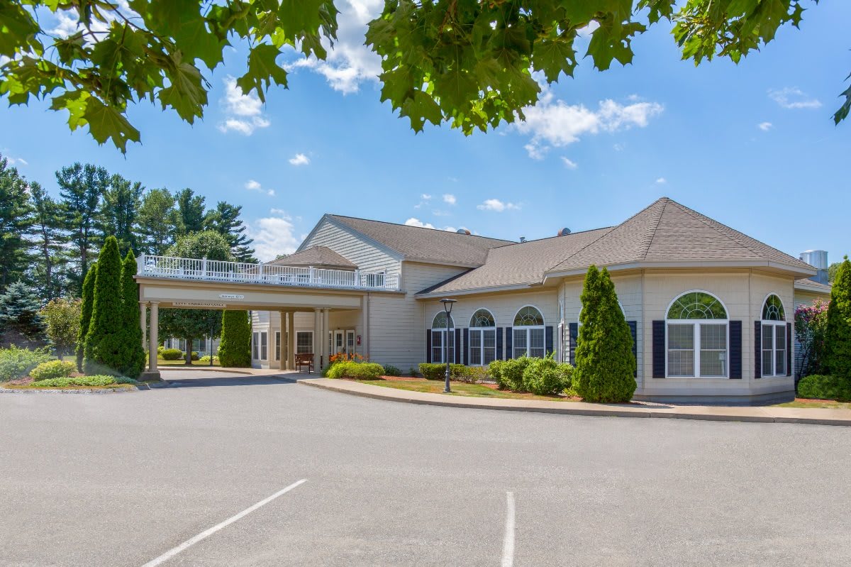 A large building with an entrance canopy and a parking lot under a partly cloudy sky.
