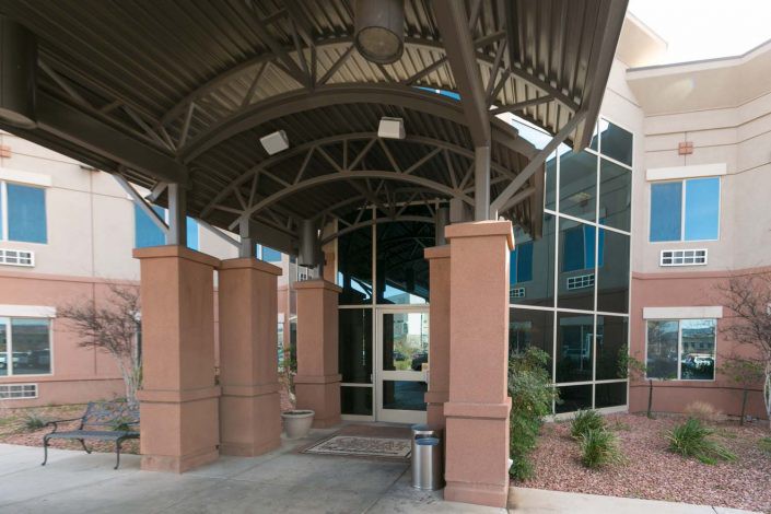 A modern building entrance with a covered walkway and large glass windows.