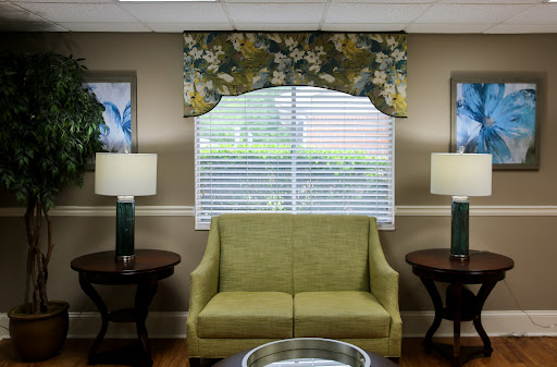 A cozy living room setting featuring a green couch, decorative lamps, and floral window treatments.