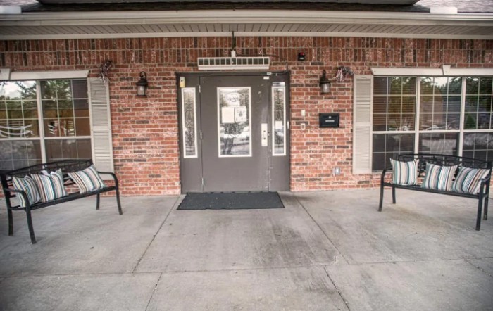 The entrance of a brick building with chairs on either side.