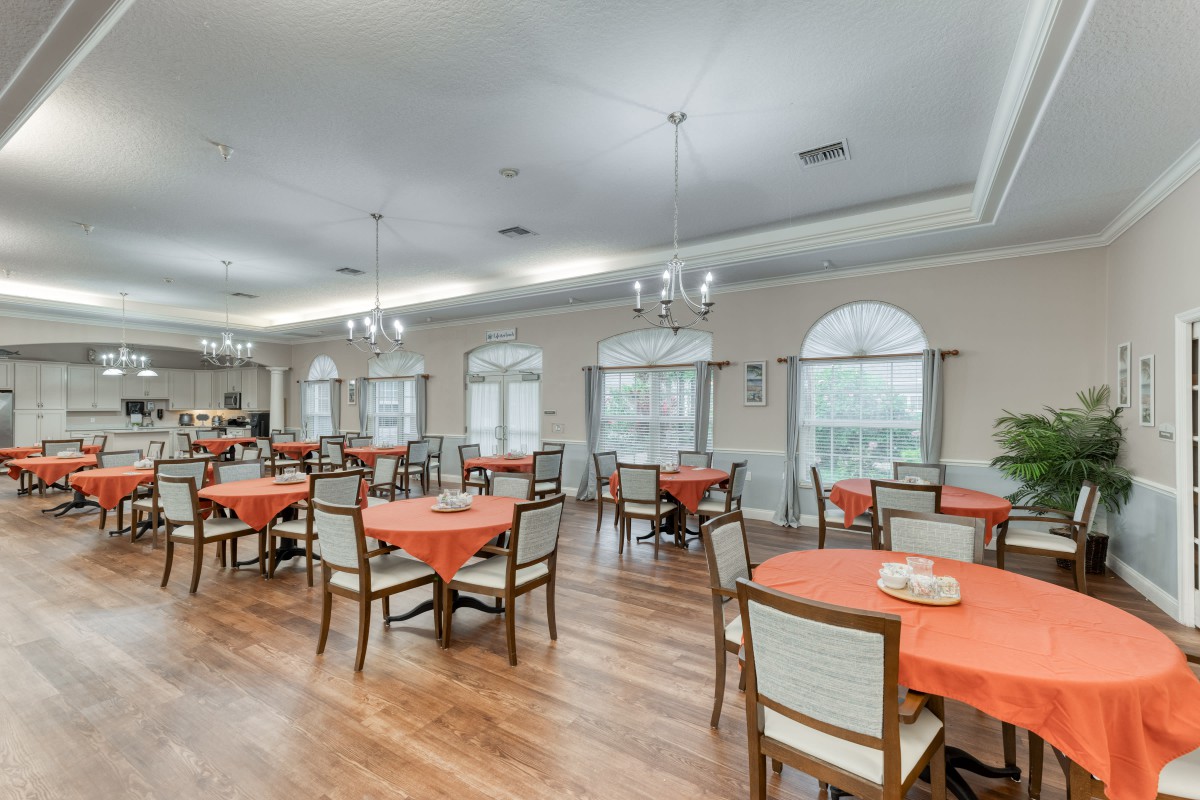 A spacious dining area with multiple tables and chairs, decorated with warm colors and chandeliers.