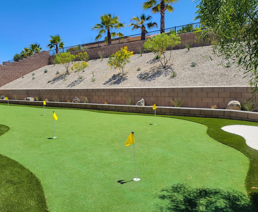 A well-maintained outdoor putting green surrounded by palm trees and desert landscaping.