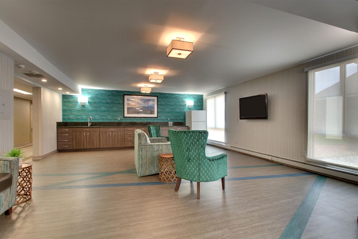 A spacious lounge with modern decor, featuring teal armchairs and a wall-mounted television.