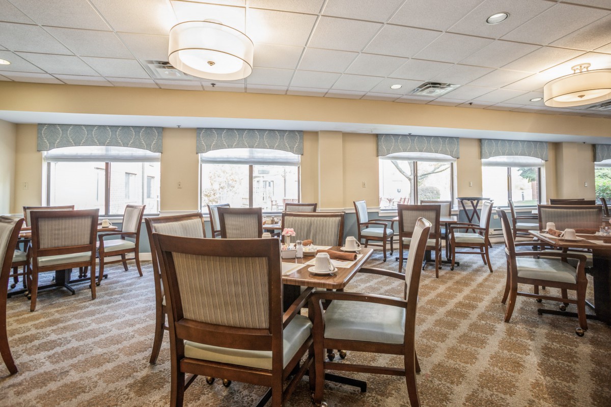 A spacious and elegantly furnished dining area with multiple tables and chairs, featuring large windows and stylish lighting.