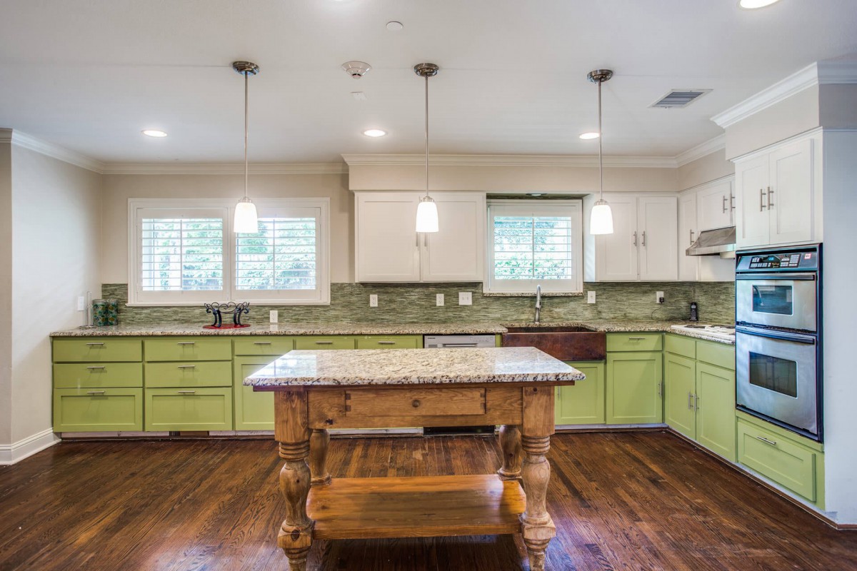 A modern kitchen with green cabinets, a wooden island, and pendant lighting.