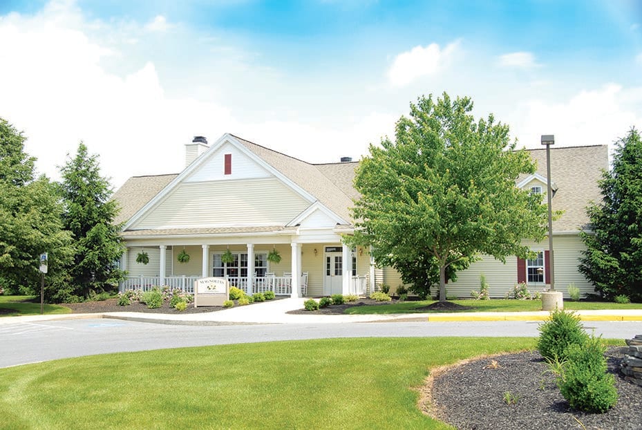 A picturesque residential building surrounded by trees and well-maintained lawns under a partly cloudy sky.