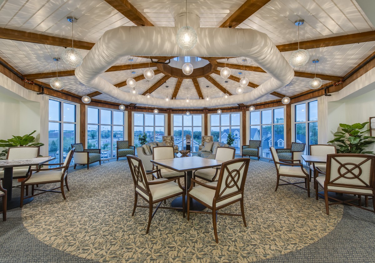 A spacious dining area with elegantly arranged tables and chairs, featuring a unique ceiling design and large windows offering an inviting ambiance.