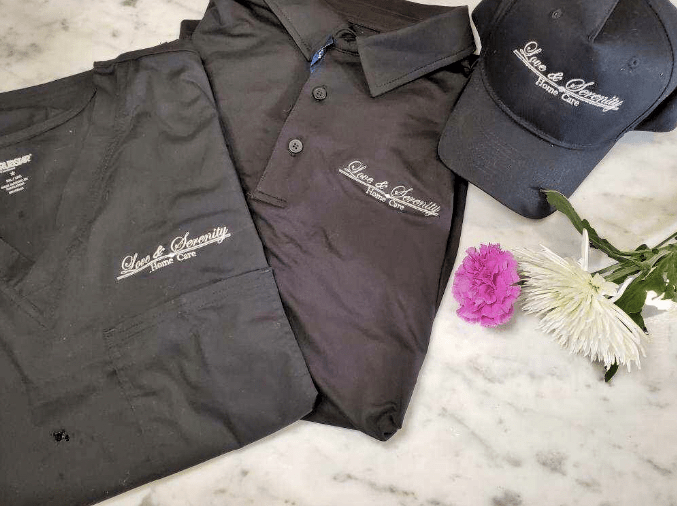 Branded uniform set featuring a polo shirt, pants, and a hat displayed on a marble surface with flowers.