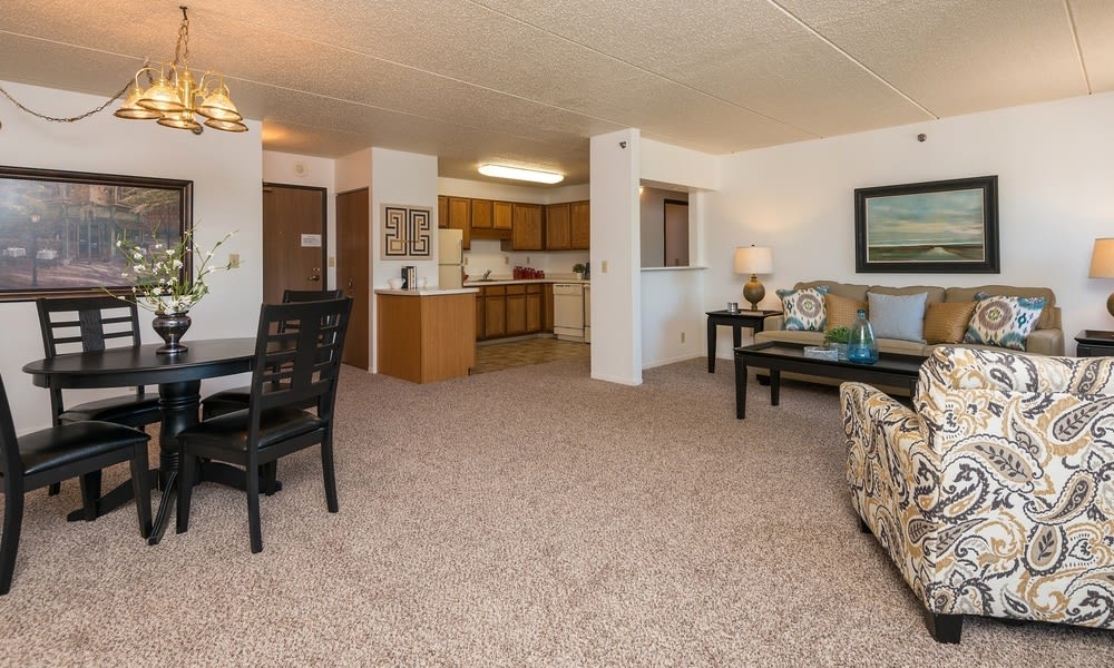 A cozy open-concept living and dining area adjacent to a kitchen with carpeted flooring.