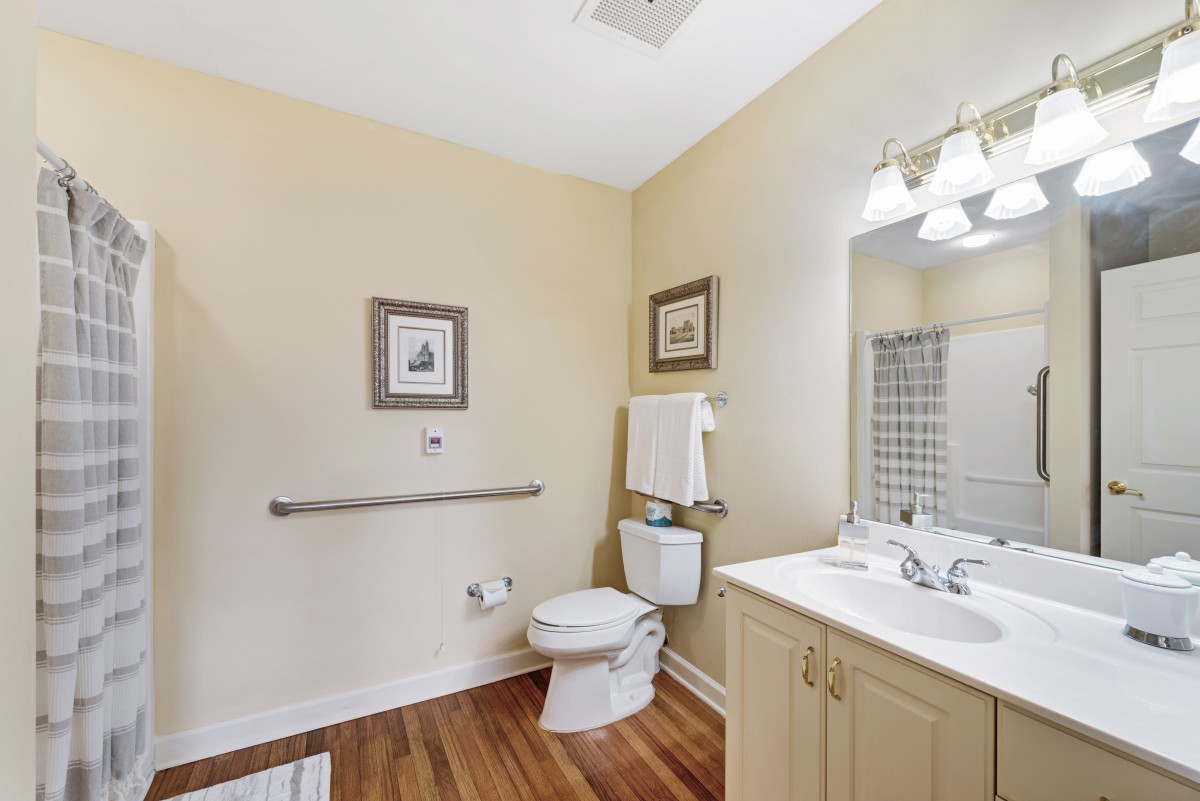A clean and well-lit bathroom with a toilet, sink, mirror, and decorative wall art.