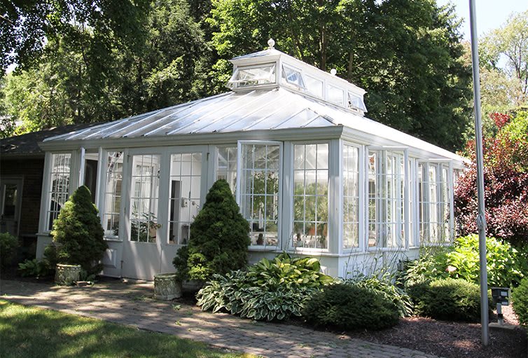 A charming glass greenhouse surrounded by lush greenery in a garden setting.