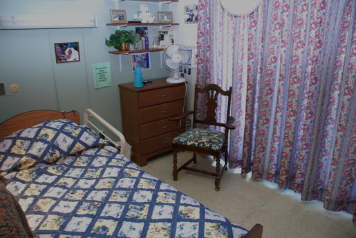 A cozy bedroom with a patterned bedspread, a wooden chair, and decorative curtains.