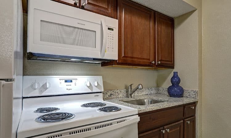 A compact kitchen with a white microwave, stovetop, wooden cabinets, and granite countertops.