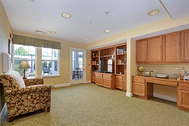 A cozy living room with built-in shelving and cabinetry, featuring comfortable seating and large windows.