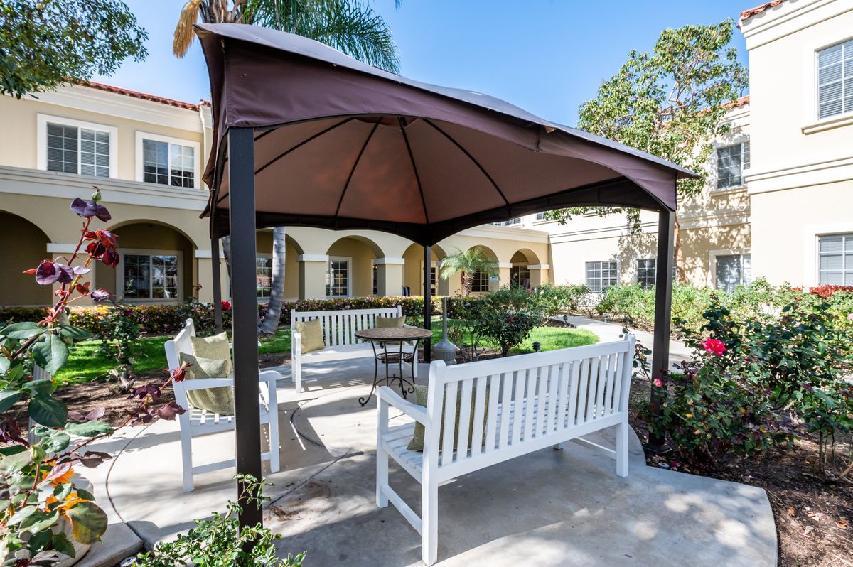 A cozy outdoor gazebo with white benches in a sunny garden setting.