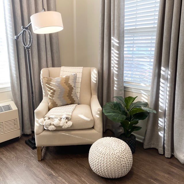A cozy corner with a comfortable armchair, soft pillows, and a blanket, complemented by an ottoman and a houseplant for a relaxing atmosphere.