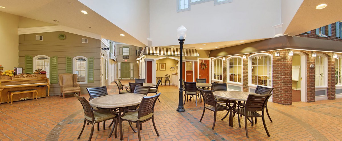 A spacious indoor area with tables and chairs, featuring a streetlamp, brick flooring, and large windows.