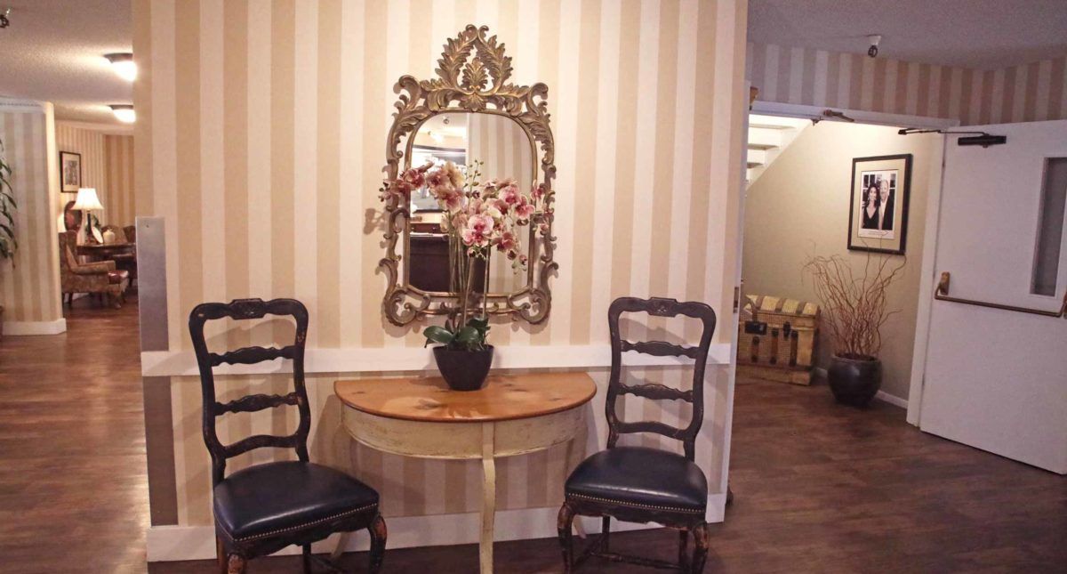 A classic interior setup featuring a decorative mirror and a table with an orchid arrangement, flanked by two elegant chairs.