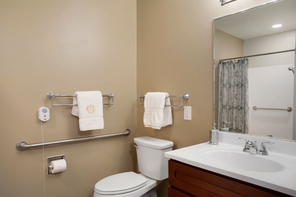 A clean and organized bathroom featuring a toilet, sink, mirror, and towels on racks.