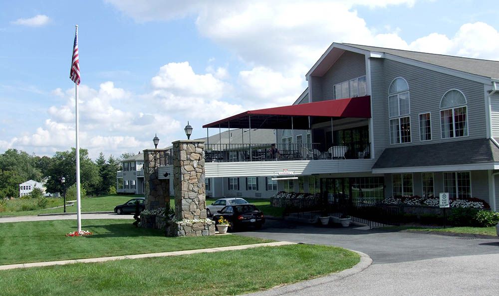A building with a red awning and stone pillar in the foreground, surrounded by a parking area and grassy landscape.